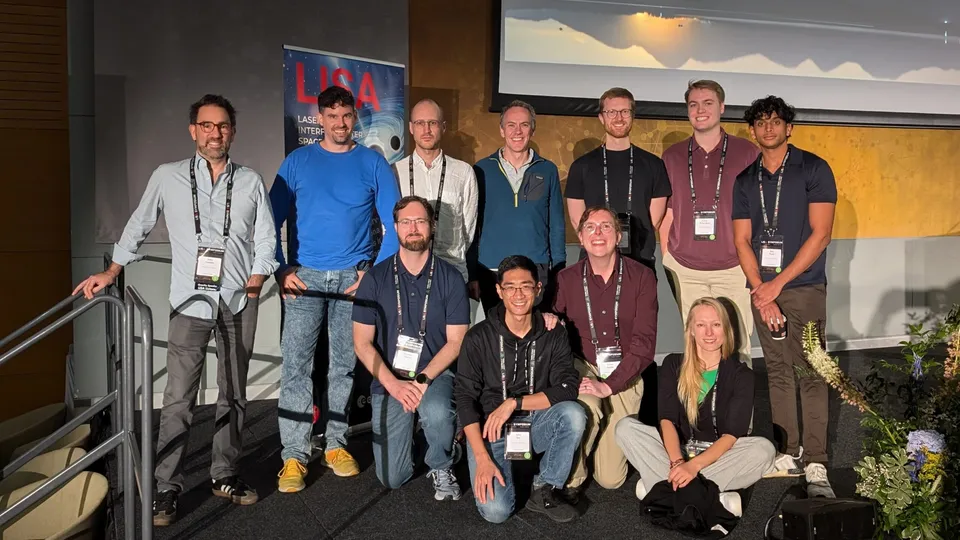 Group photo of the PSSL team at a  ympo ium, with eleven member   tanding and kneeling in front of a LISA po ter. They are wearing conference badge  and are in a well-lit room with a projector  creen behind them.